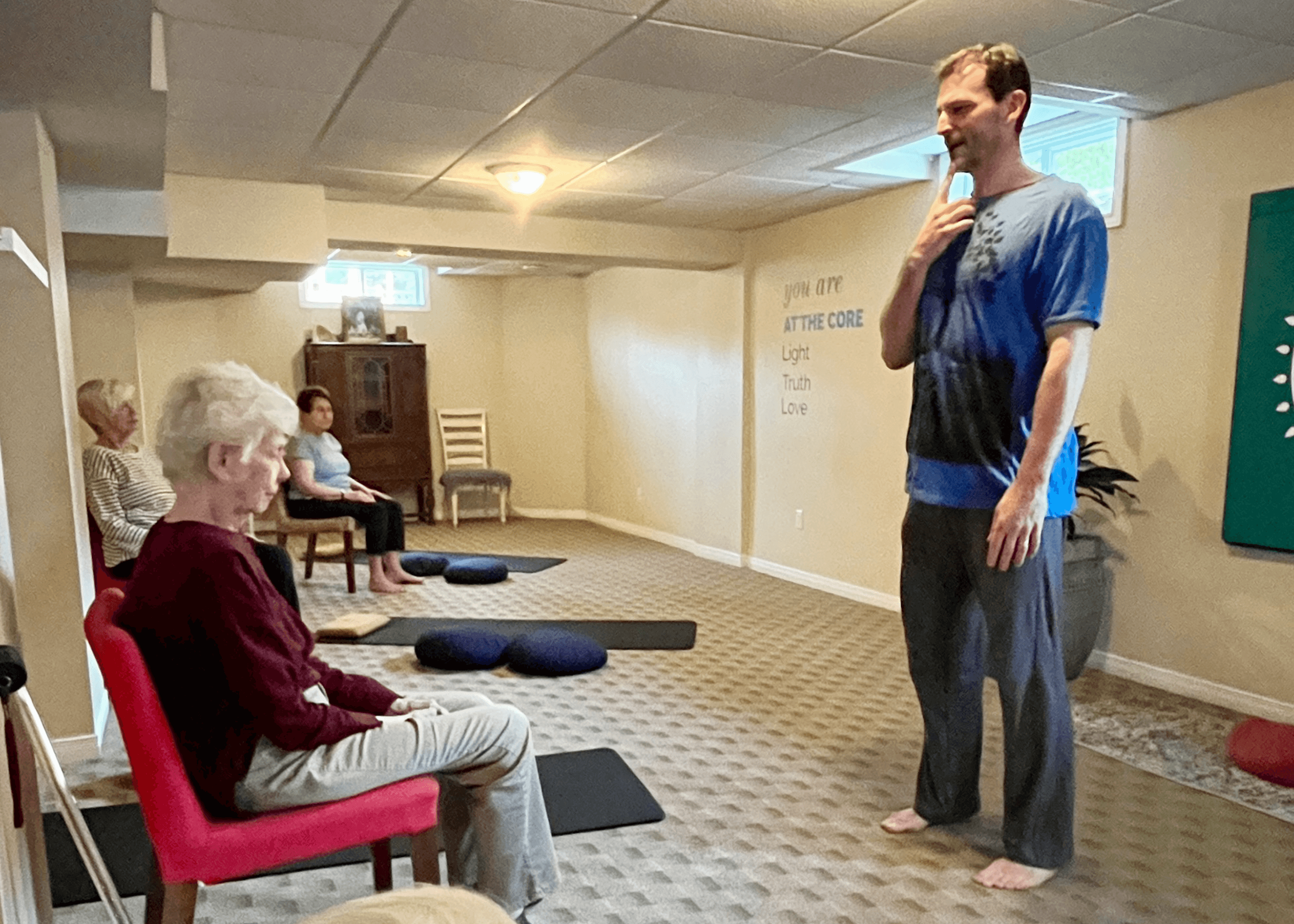 A small group of older adults participating in a gentle yoga class, using chairs and props for support, guided by an instructor in a bright, welcoming studio.