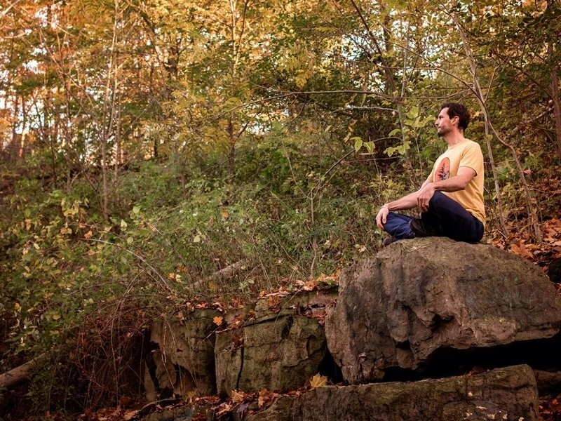 Man sitting cross-legged on a rock in the forest during autumn, representing accessible meditation classes in London ON.