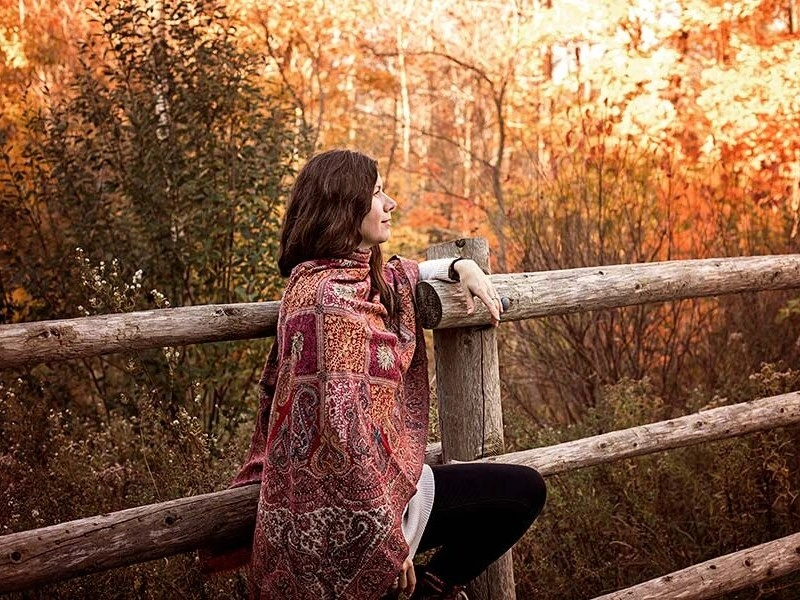Shankari resting on a wooden fence wrapped in a shawl, symbolizing the introspective nature of London Ontario meditation classes.